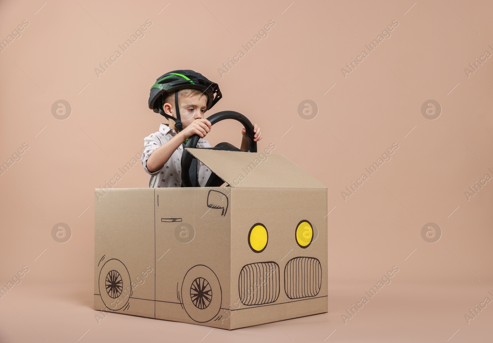 Photo of Little boy driving car made of cardboard on beige background. Space for text