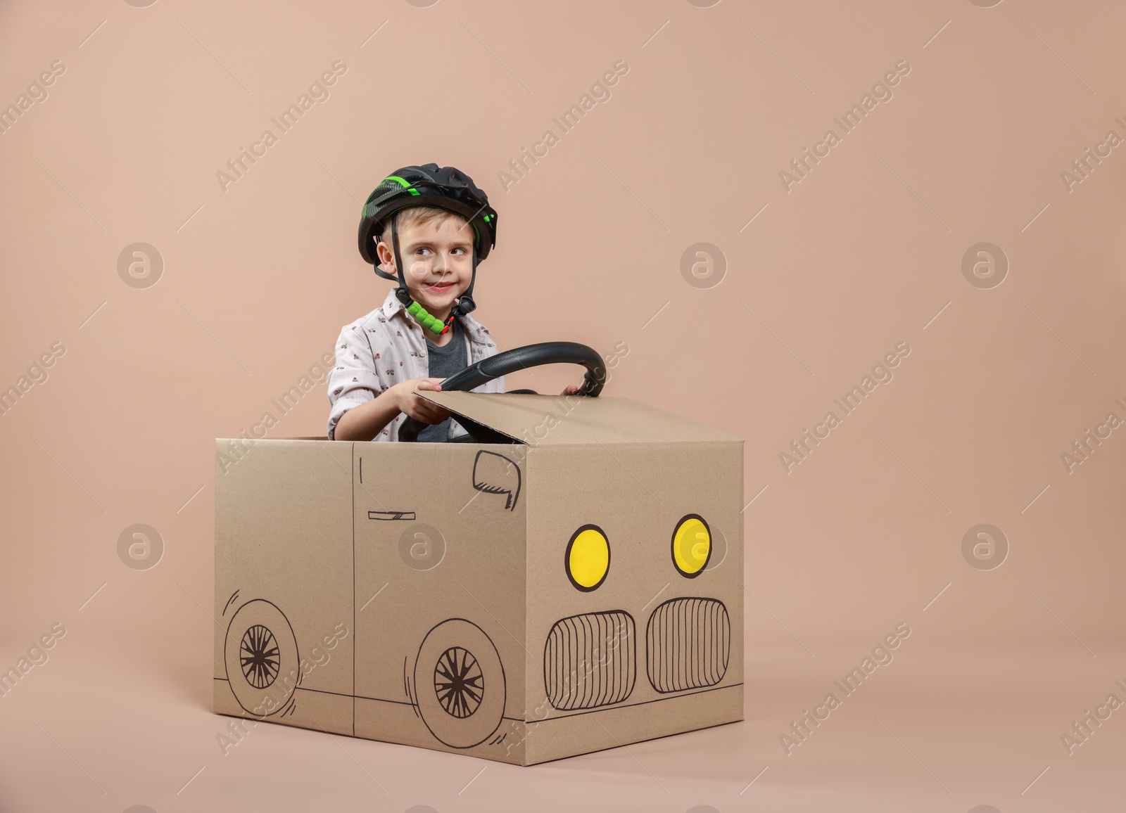 Photo of Little boy driving car made of cardboard on beige background. Space for text