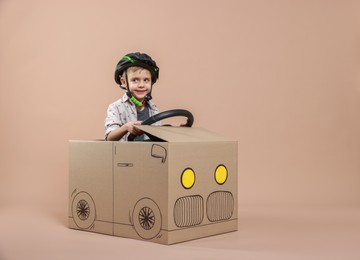 Photo of Little boy driving car made of cardboard on beige background. Space for text