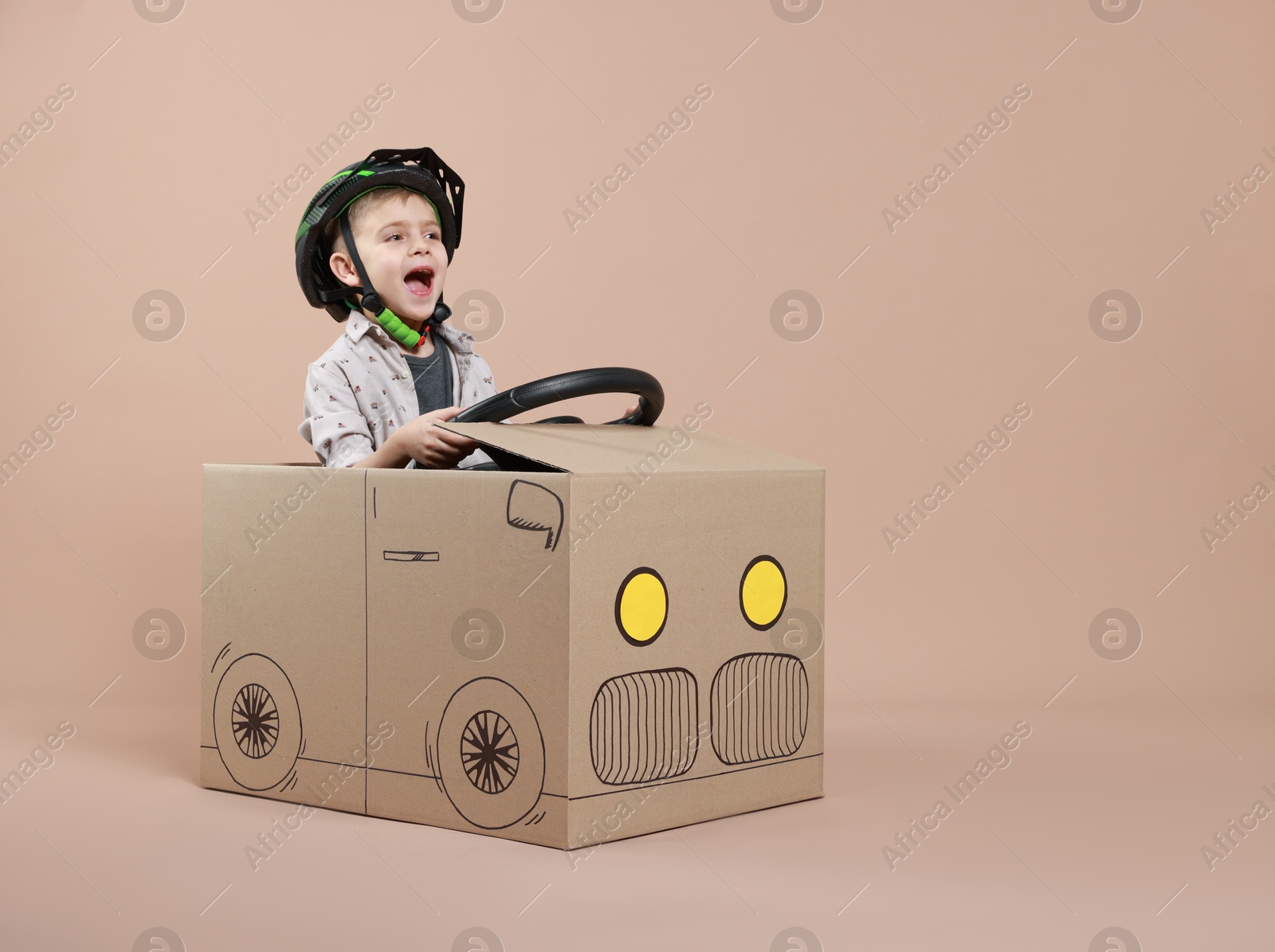 Photo of Little boy driving car made of cardboard on beige background. Space for text