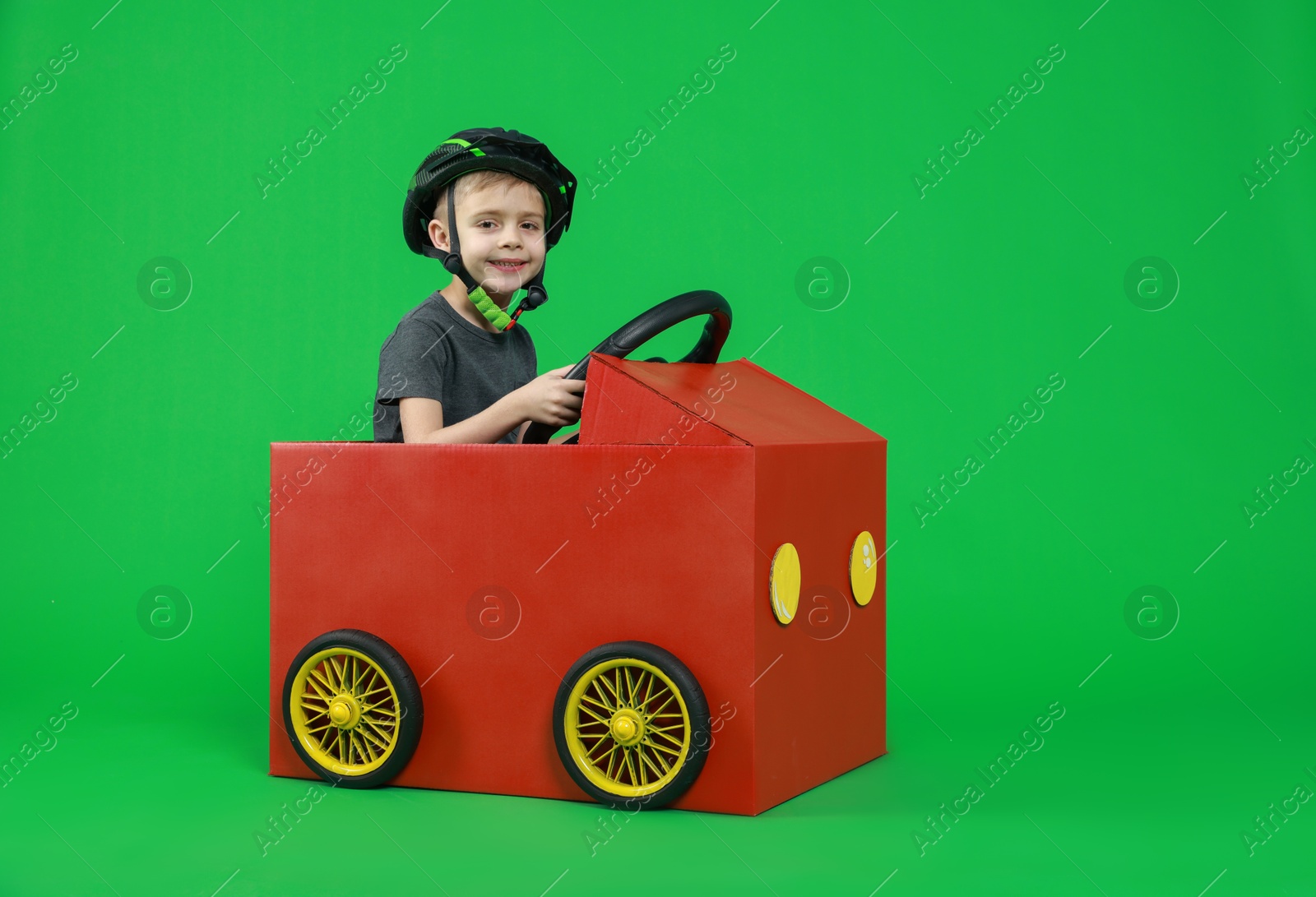 Photo of Little boy driving car made of cardboard on green background