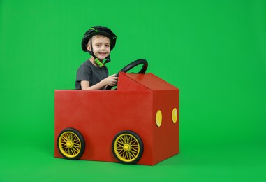 Photo of Little boy driving car made of cardboard on green background