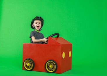 Photo of Little boy driving car made of cardboard on green background. Space for text