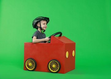 Photo of Little boy driving car made of cardboard on green background. Space for text