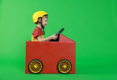 Photo of Little boy driving car made of cardboard on green background. Space for text