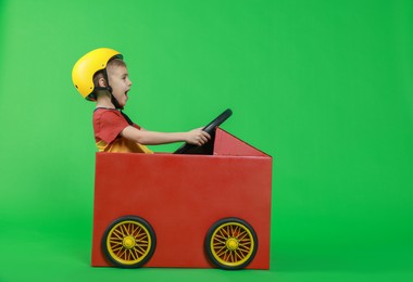 Photo of Little boy driving car made of cardboard on green background. Space for text