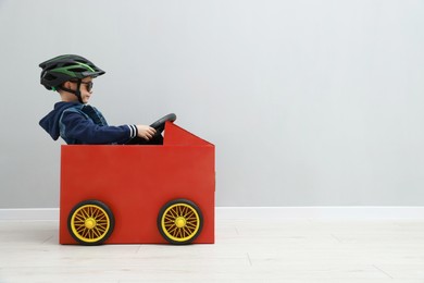 Photo of Little boy driving car made of cardboard against light wall. Space for text