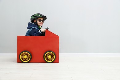 Photo of Little boy driving car made of cardboard against light wall. Space for text