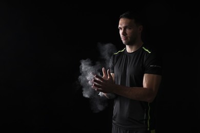 Photo of Man clapping hands with talcum powder before training on black background. Space for text