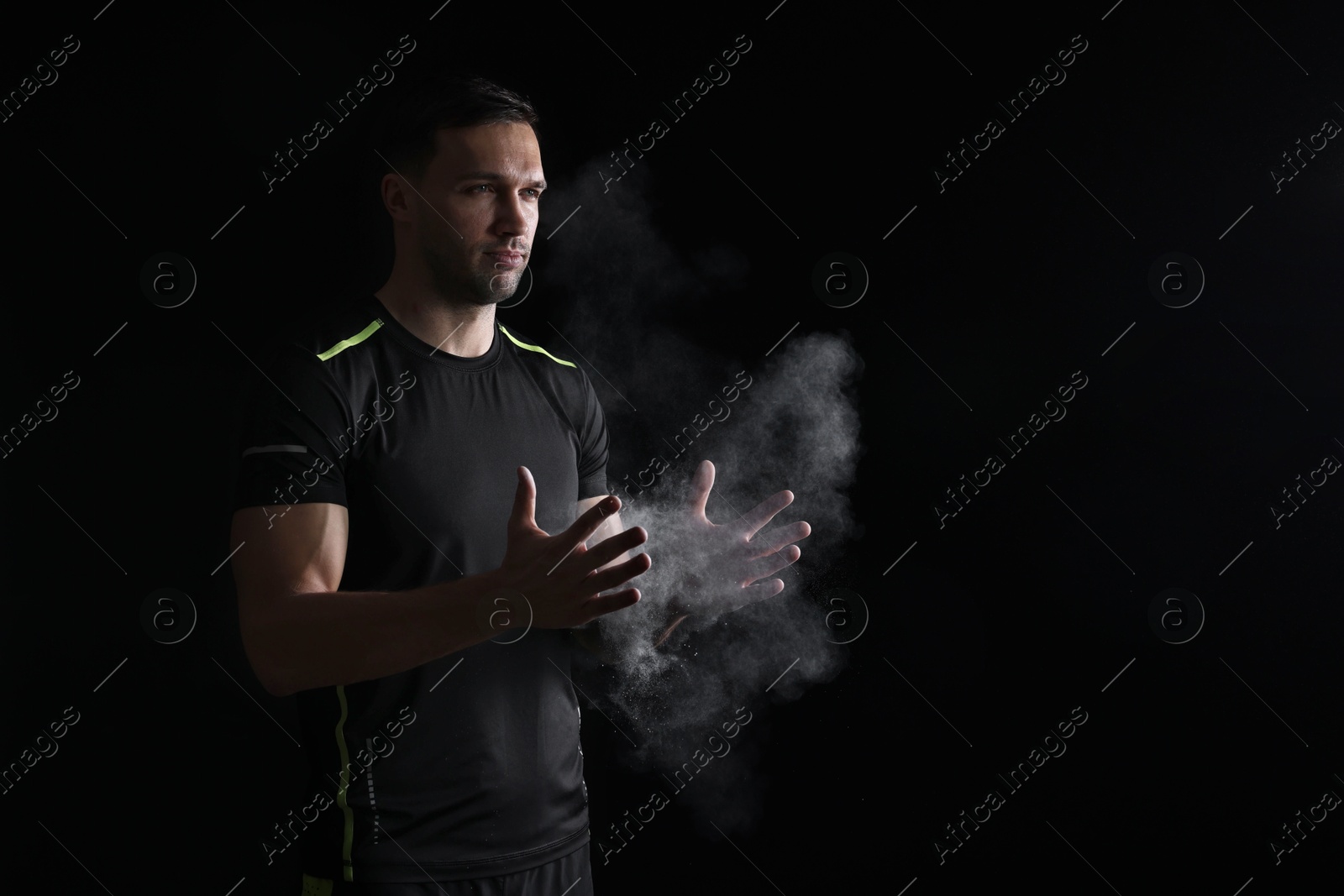 Photo of Man clapping hands with talcum powder before training on black background. Space for text