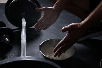 Photo of Man applying talcum powder onto his hands above bowl before training with barbell in gym, closeup