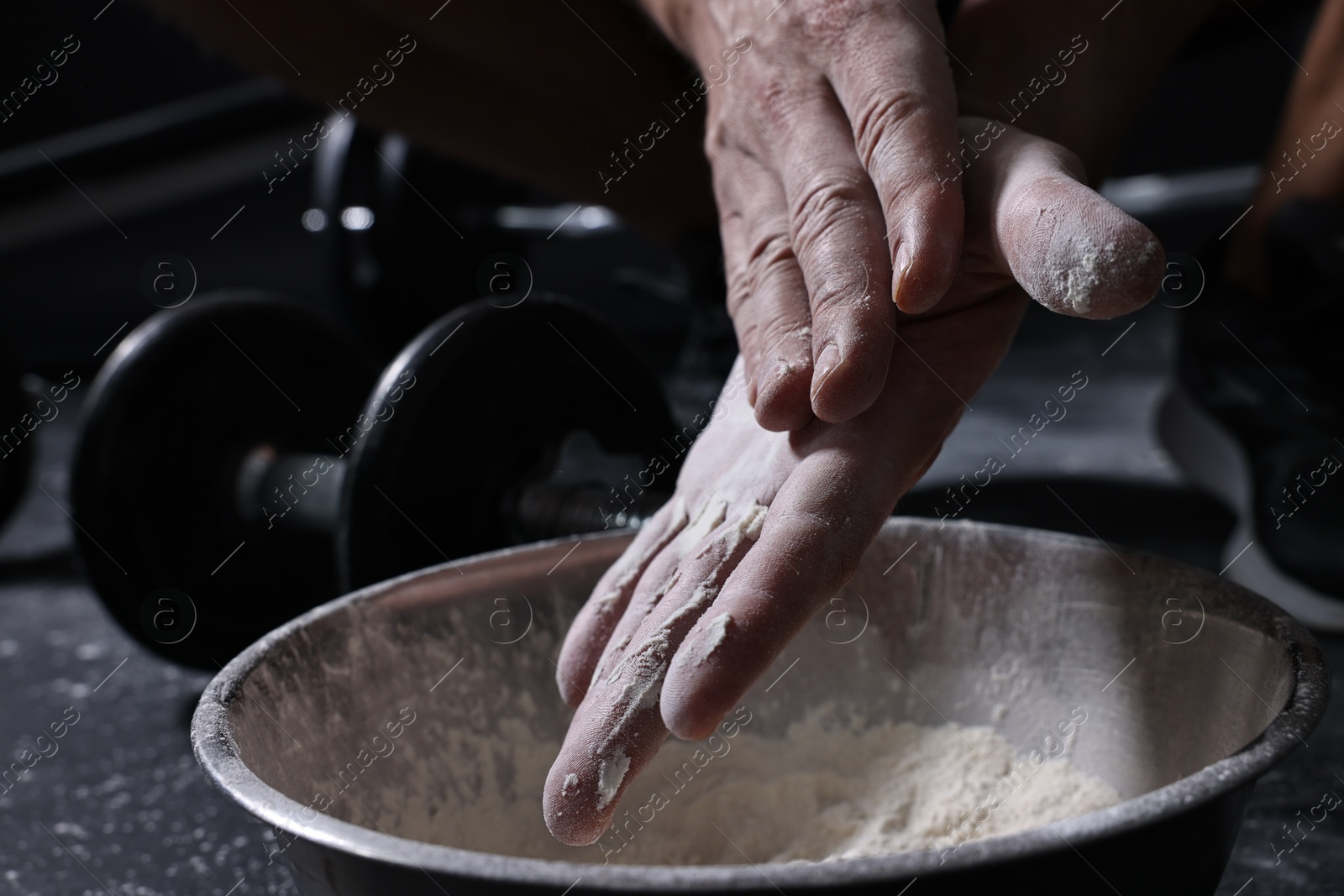 Photo of Man applying talcum powder onto his hands above bowl before training in gym, closeup