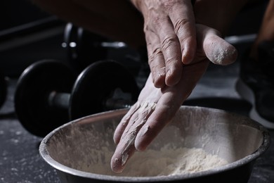 Photo of Man applying talcum powder onto his hands above bowl before training in gym, closeup