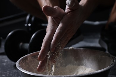 Photo of Man applying talcum powder onto his hands above bowl before training in gym, closeup