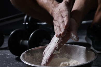 Photo of Man applying talcum powder onto his hands above bowl before training in gym, closeup