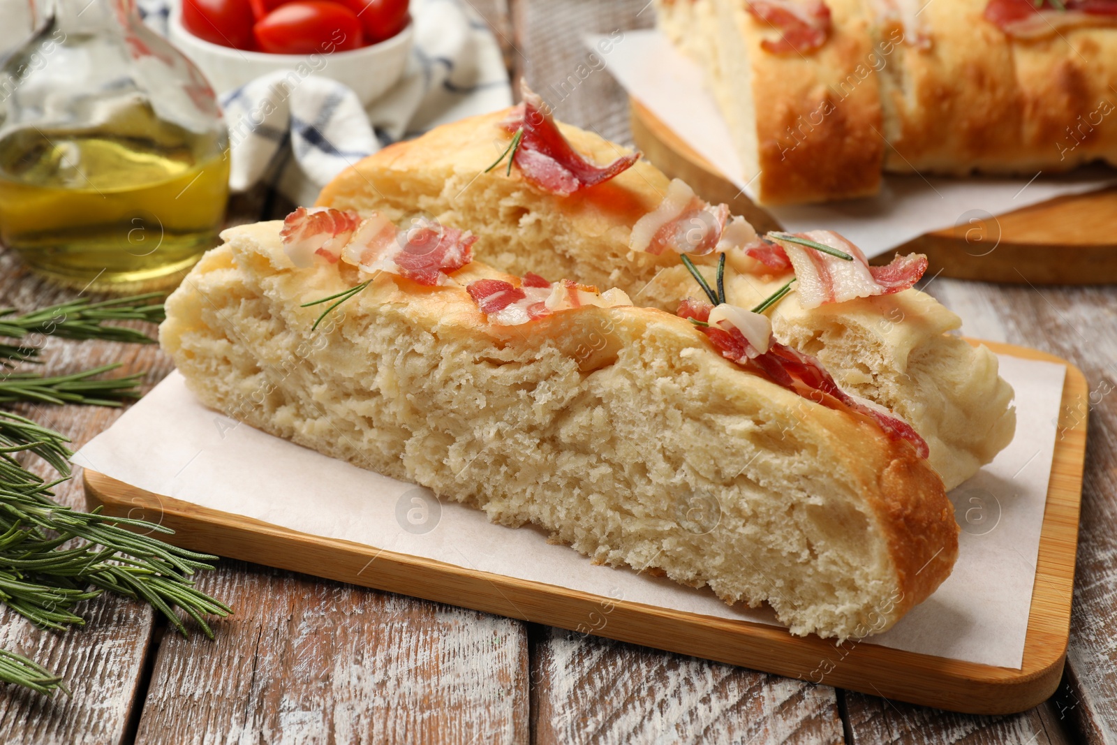 Photo of Slices of delicious focaccia bread with bacon and rosemary on wooden table, closeup