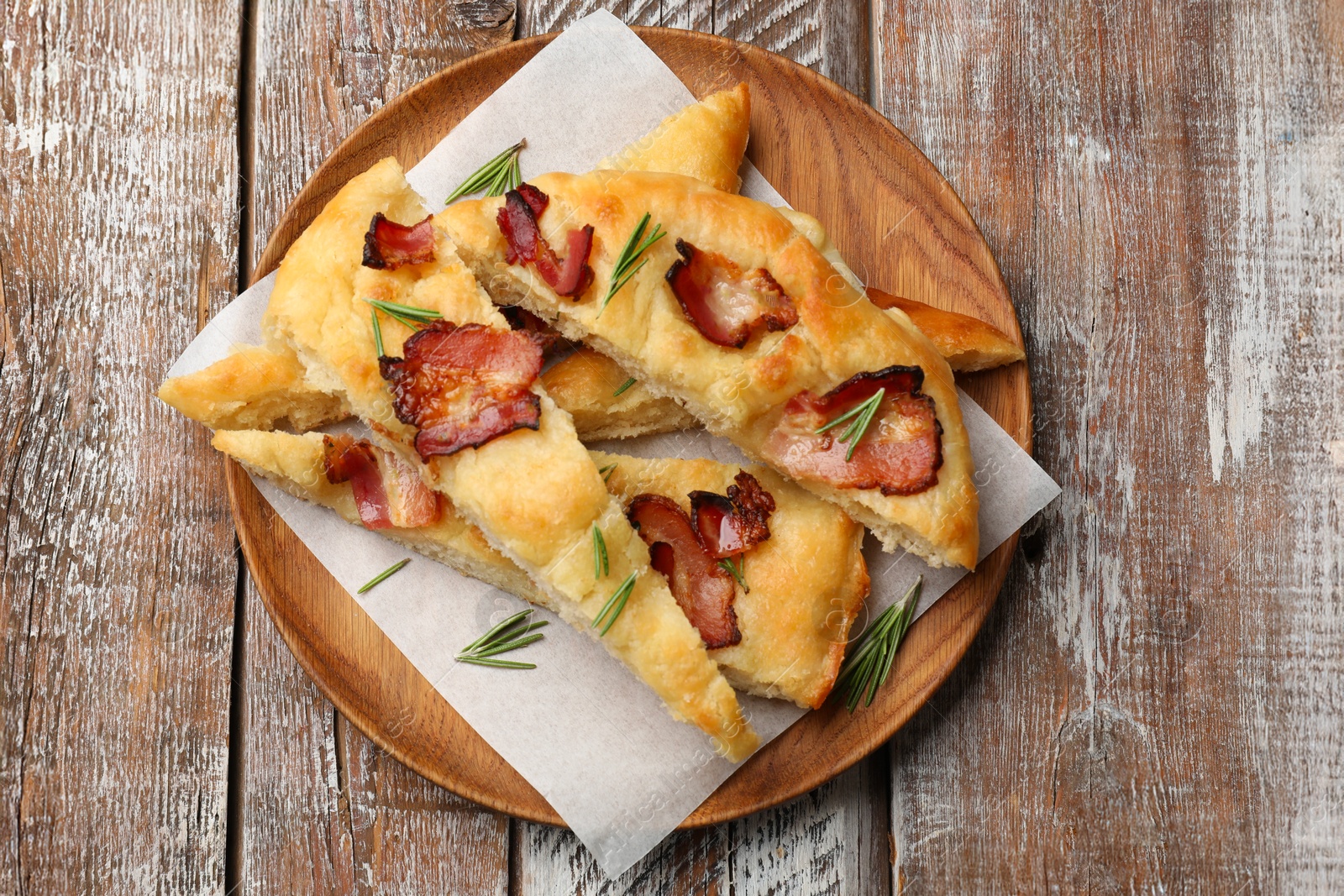 Photo of Slices of delicious focaccia bread with bacon and rosemary on wooden table, top view