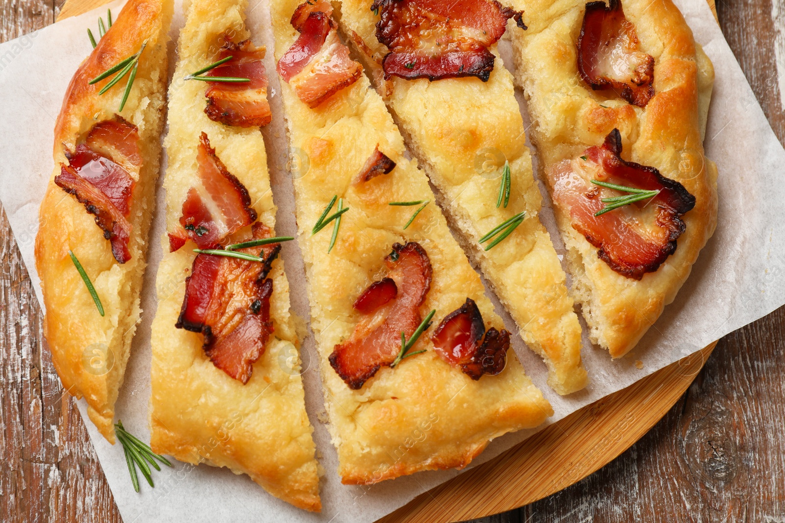 Photo of Slices of delicious focaccia bread with bacon and rosemary on wooden table, top view