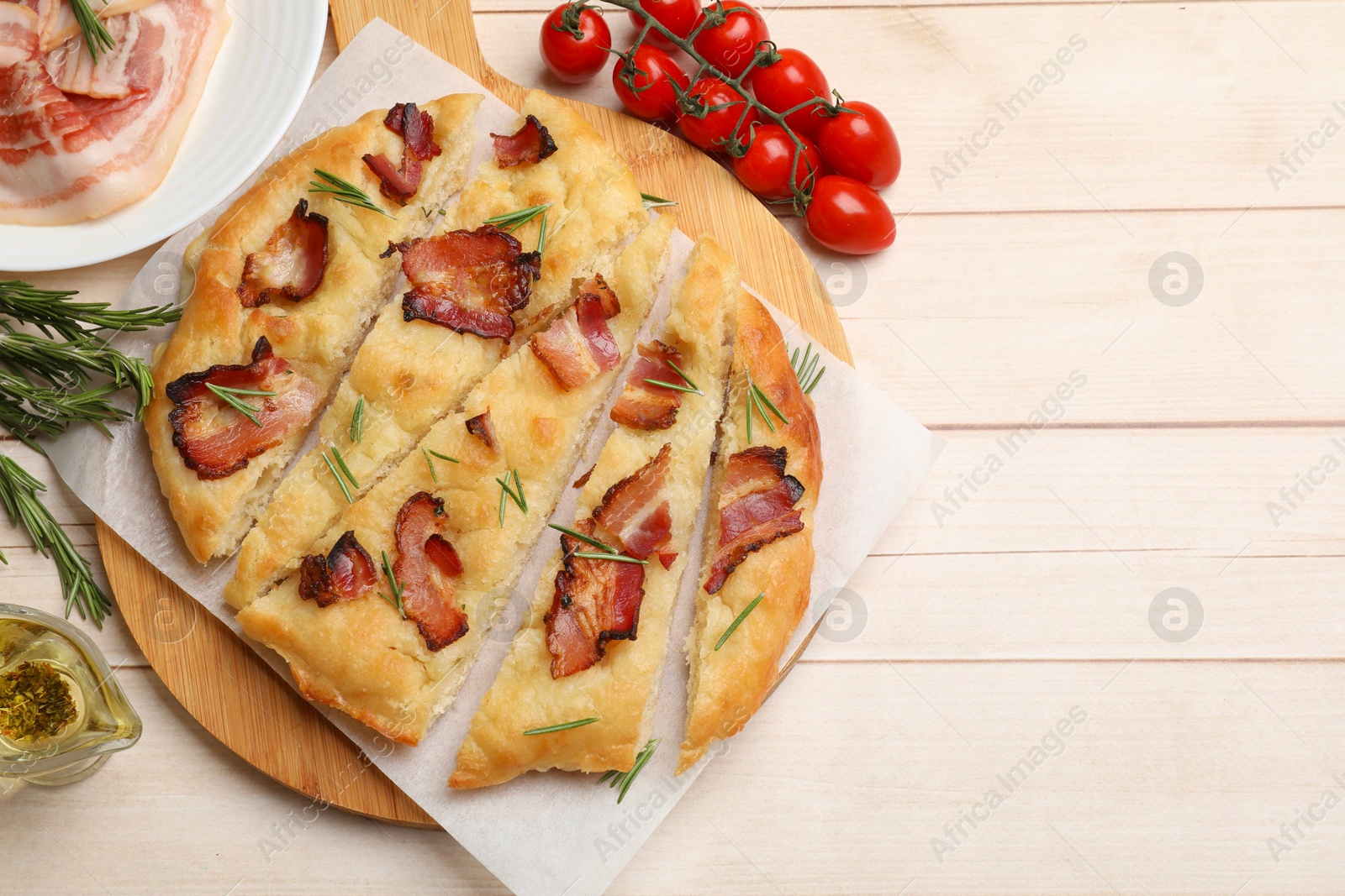 Photo of Slices of delicious focaccia bread with bacon, rosemary, oil and tomatoes on wooden table, flat lay. Space for text