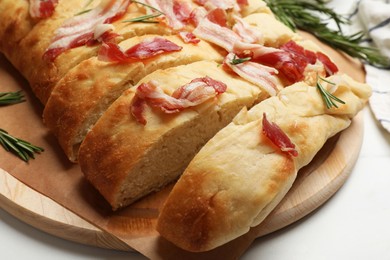 Photo of Slices of delicious focaccia bread with bacon and rosemary on white table, closeup