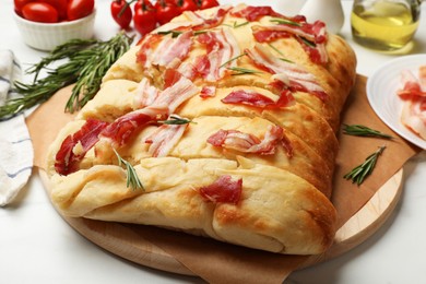 Photo of Slices of delicious focaccia bread with bacon, rosemary, oil and tomatoes on white table, closeup