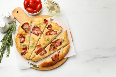 Photo of Slices of delicious focaccia bread with bacon, rosemary, oil and tomatoes on white marble table, flat lay. Space for text