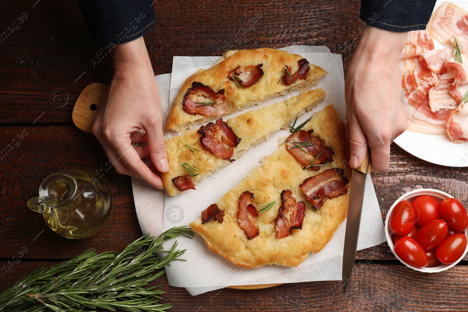 Photo of Woman with knife taking slice of delicious focaccia bread at wooden table, top view