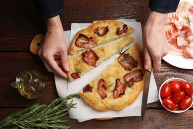 Photo of Woman with knife taking slice of delicious focaccia bread at wooden table, top view