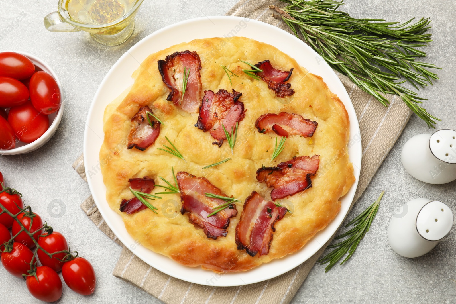 Photo of Delicious focaccia bread with bacon, rosemary, tomatoes and oil on light grey table, flat lay