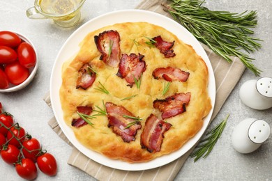 Photo of Delicious focaccia bread with bacon, rosemary, tomatoes and oil on light grey table, flat lay