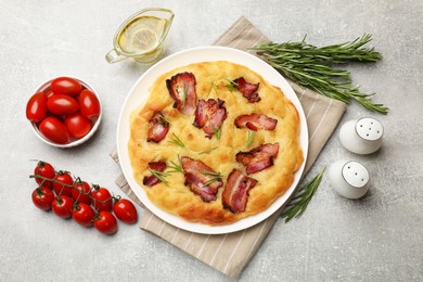 Photo of Delicious focaccia bread with bacon, rosemary, tomatoes and oil on light grey table, flat lay