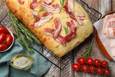 Photo of Delicious focaccia bread with bacon, rosemary, oil and tomatoes on wooden table, flat lay