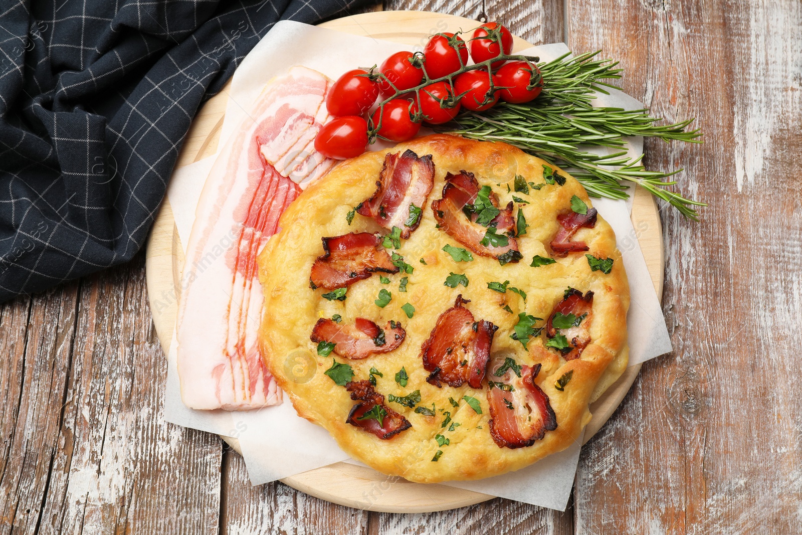 Photo of Delicious focaccia bread with bacon, parsley, tomatoes and rosemary on wooden table, top view