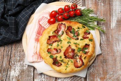 Photo of Delicious focaccia bread with bacon, parsley, tomatoes and rosemary on wooden table, top view