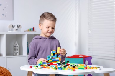 Photo of Cute boy playing with building blocks at white table indoors. Space for text