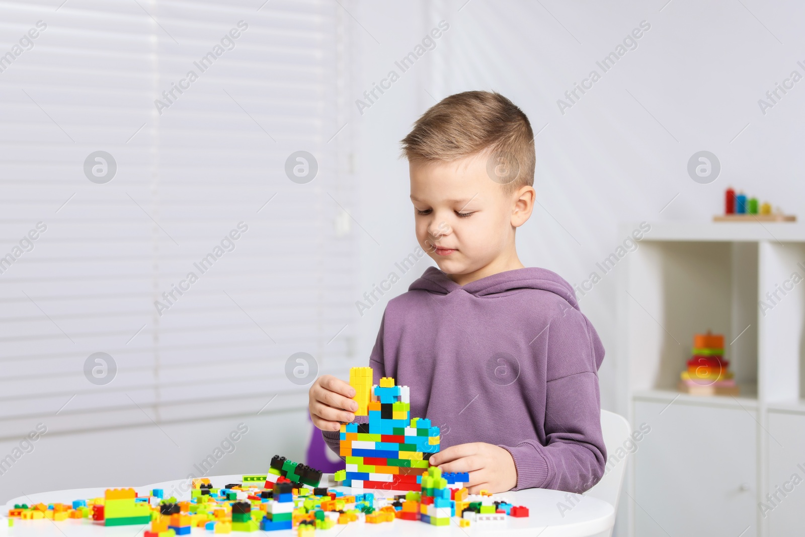 Photo of Cute boy playing with building blocks at white table indoors. Space for text