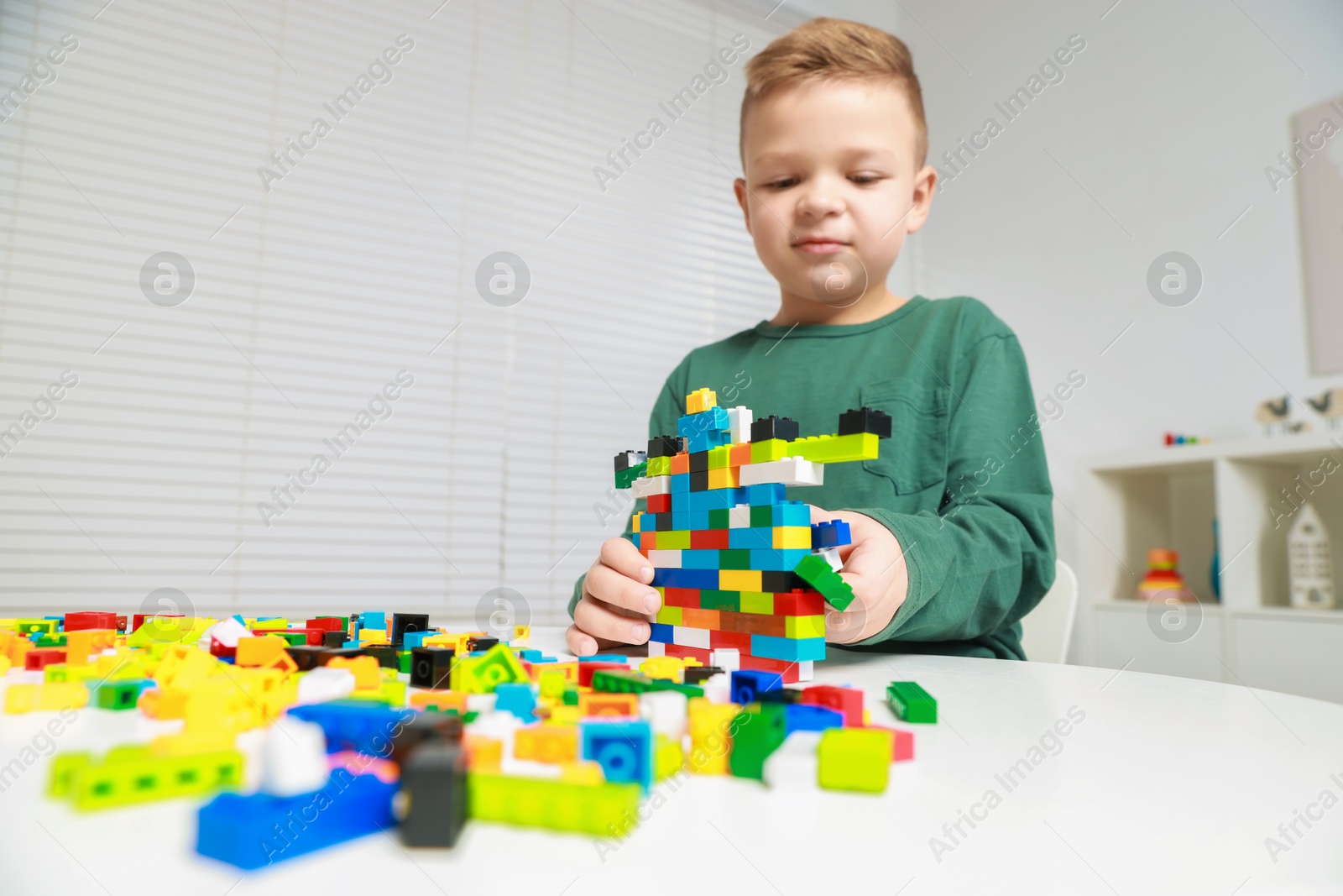 Photo of Cute boy playing with building blocks at white table indoors, low angle view