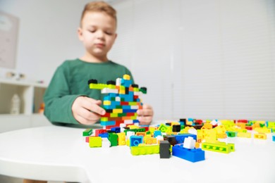 Photo of Cute boy playing with building blocks at white table indoors, selective focus