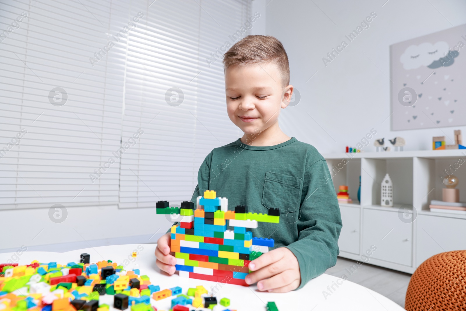 Photo of Cute boy playing with building blocks at white table indoors. Space for text