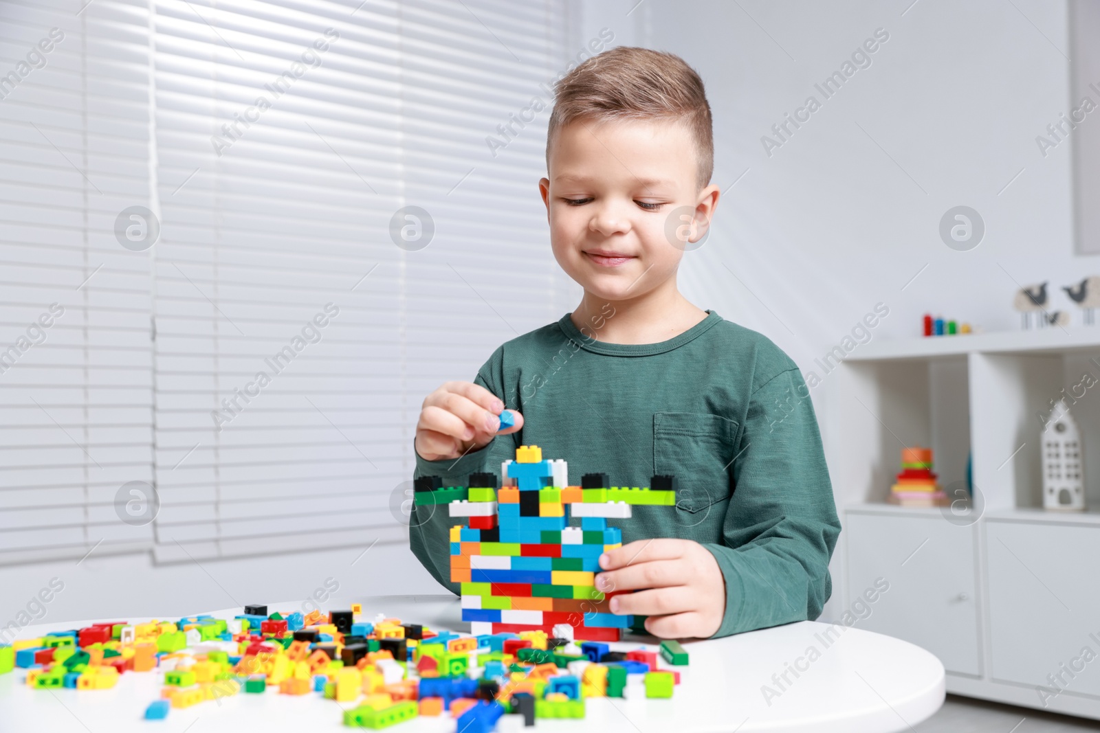 Photo of Cute boy playing with building blocks at white table indoors. Space for text