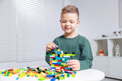 Photo of Cute boy playing with building blocks at white table indoors. Space for text