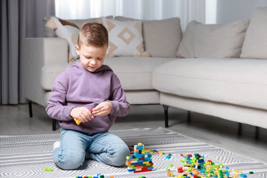 Photo of Cute boy playing with building blocks on floor at home. Space for text