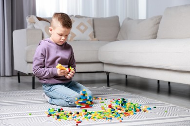 Photo of Cute boy playing with building blocks on floor at home. Space for text