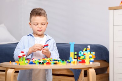 Photo of Cute boy playing with building blocks at wooden table indoors