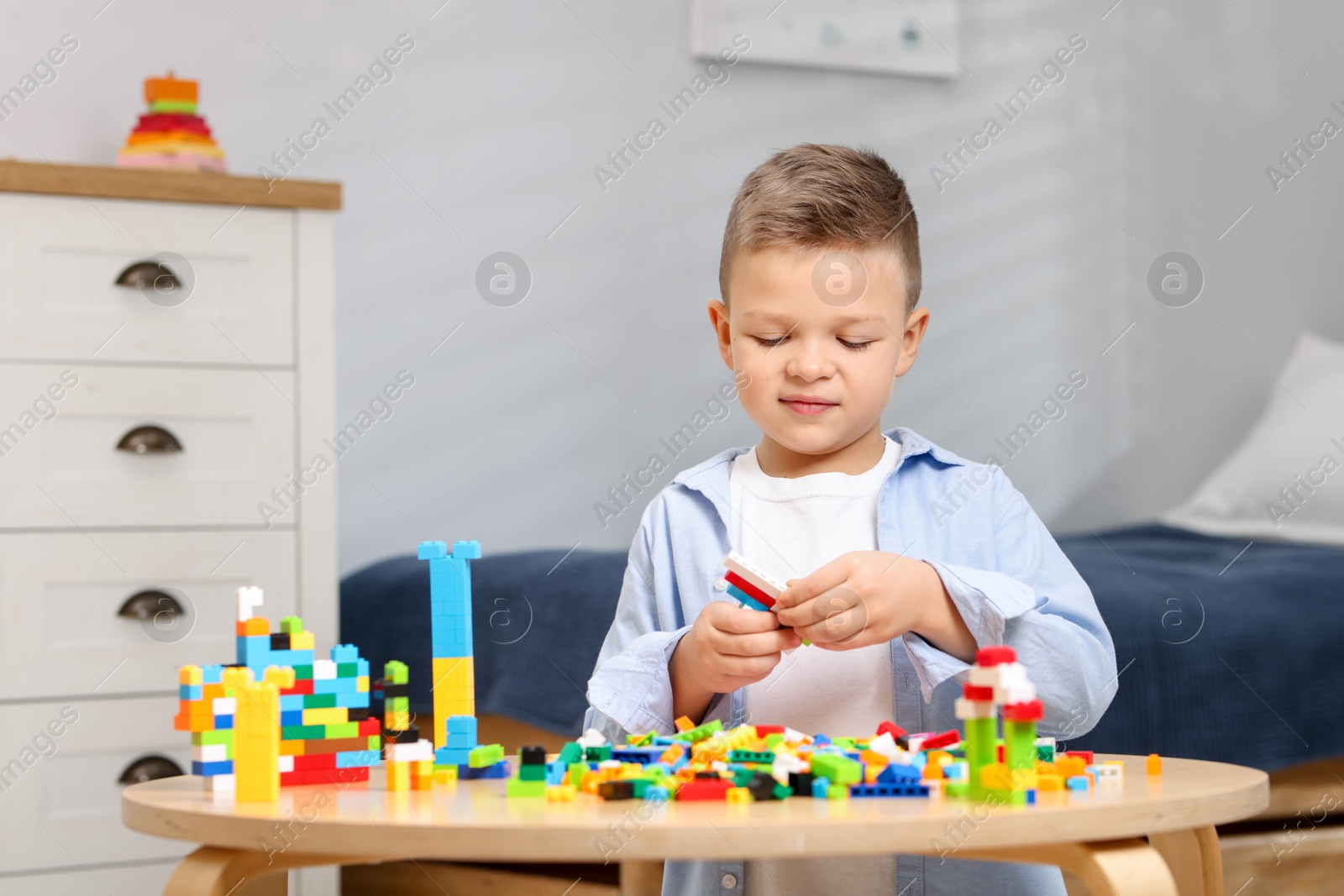 Photo of Cute boy playing with building blocks at wooden table indoors