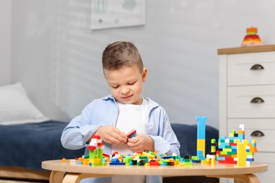 Photo of Cute boy playing with building blocks at wooden table indoors