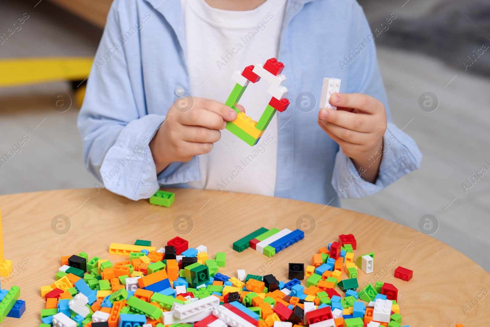 Photo of Cute boy playing with building blocks at wooden table indoors, closeup