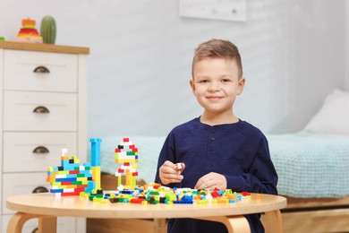 Photo of Cute boy playing with building blocks at wooden table indoors