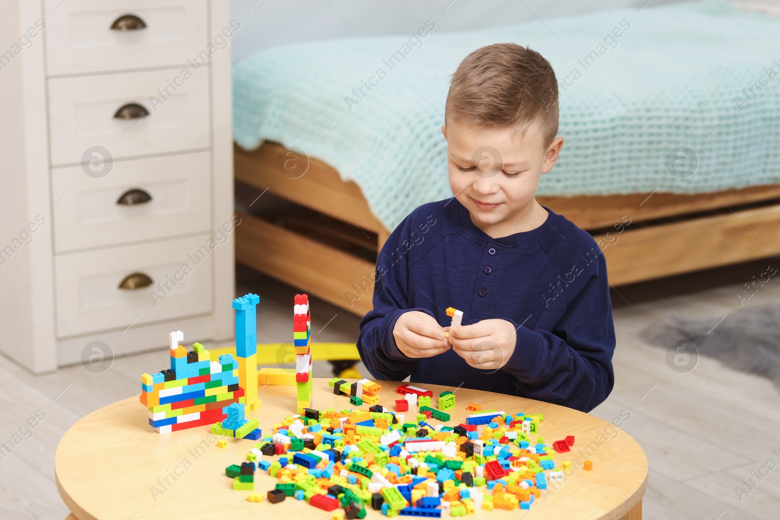 Photo of Cute boy playing with building blocks at wooden table indoors