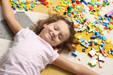 Photo of Cute girl lying near building blocks on carpet at home